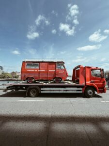 A car being loaded onto an open vehicle transport trailer by a worker on a suburban street.