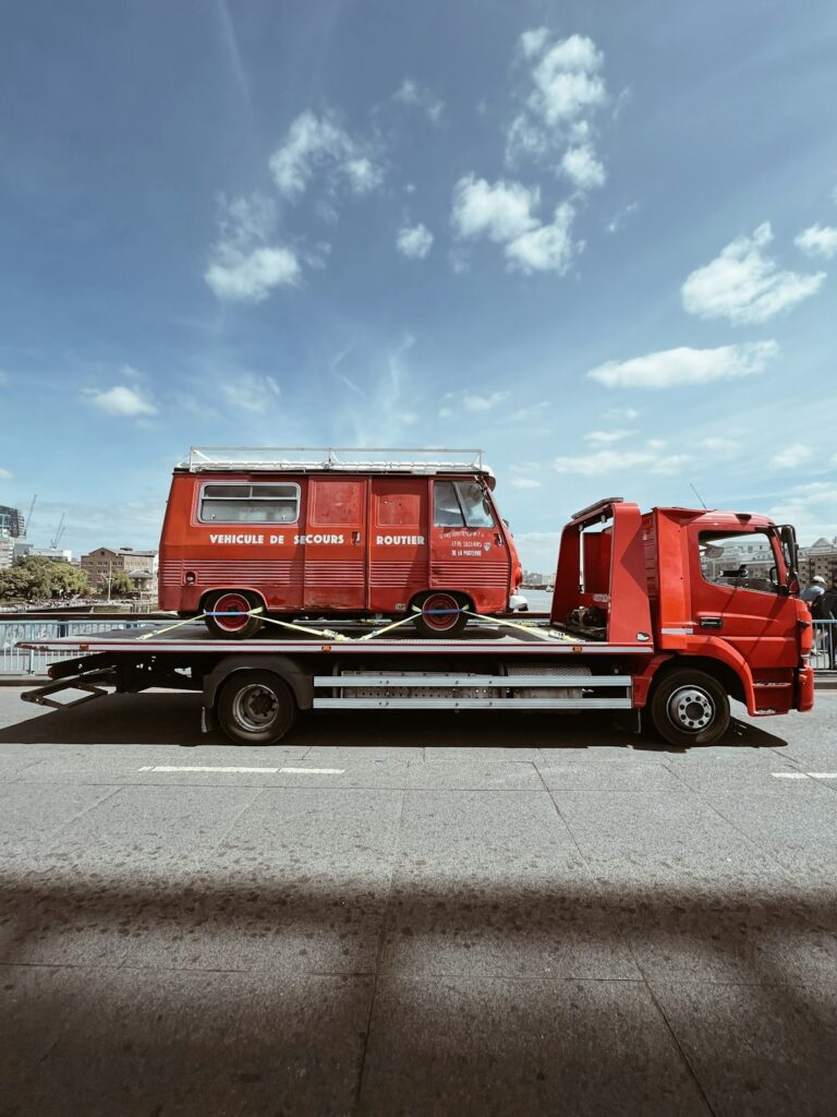 A car being loaded onto an open vehicle transport trailer by a worker on a suburban street.