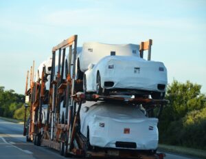 A vintage car being carefully loaded onto an enclosed vehicle transport trailer by two workers.