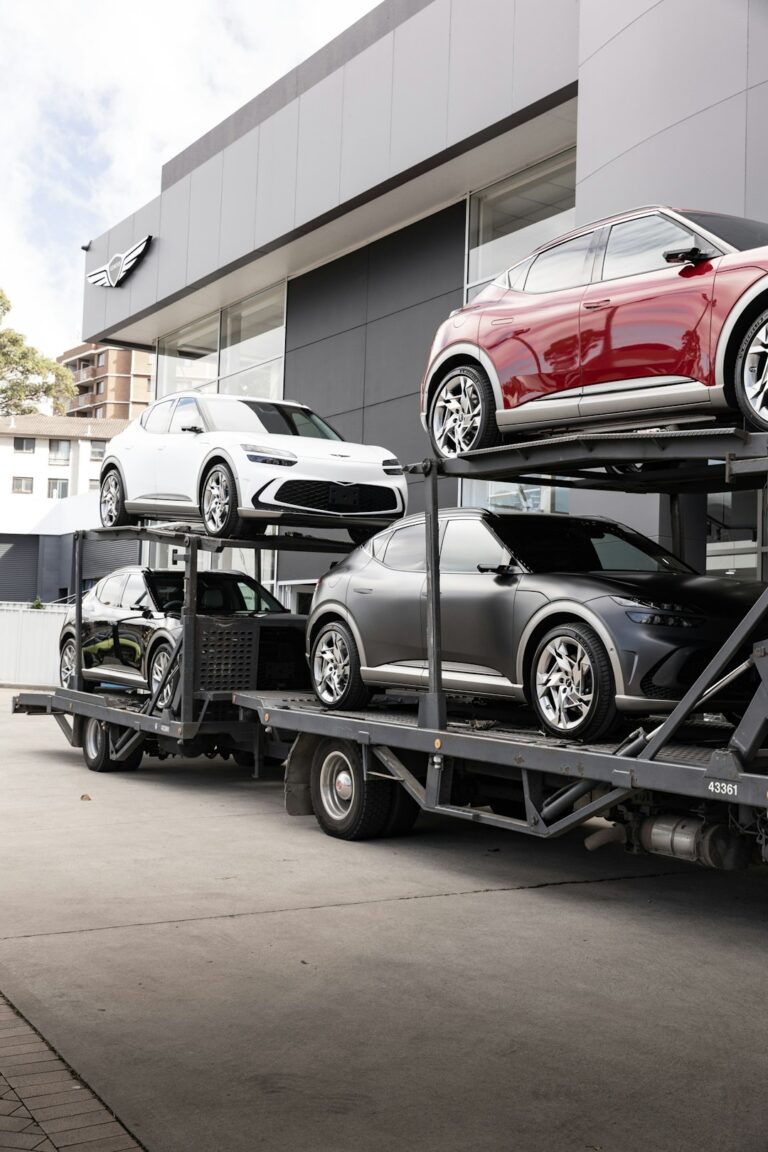 A sedan loaded onto an open transport trailer with a few visible bags in the back seat.