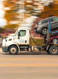 A car being loaded onto a multi-level transport truck by a driver on a residential street.